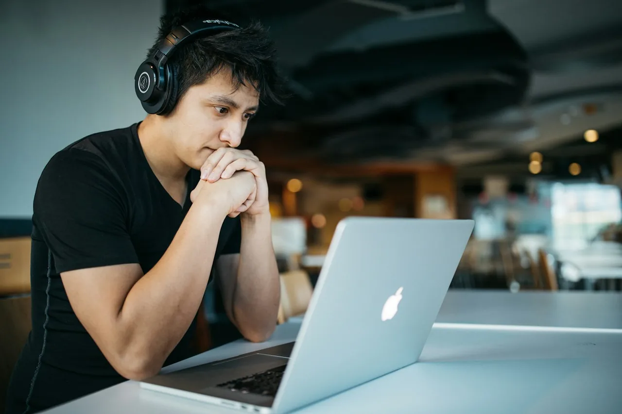 An adult wearing headphones while studying at a laptop.