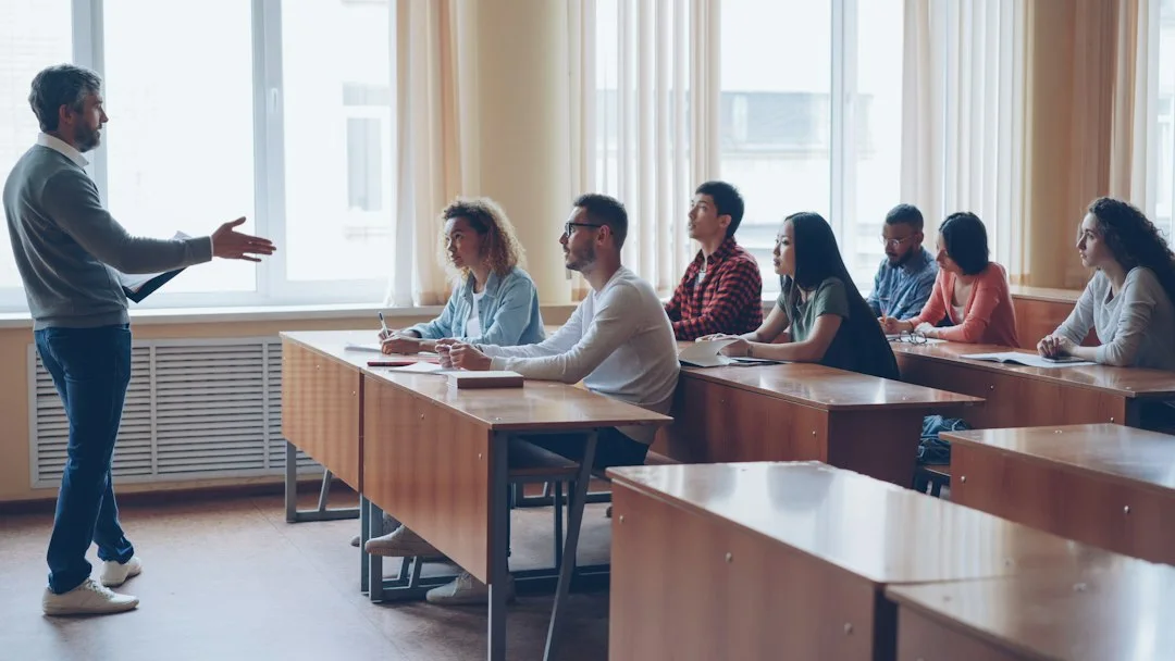 Adults listening and taking notes at classroom tables.