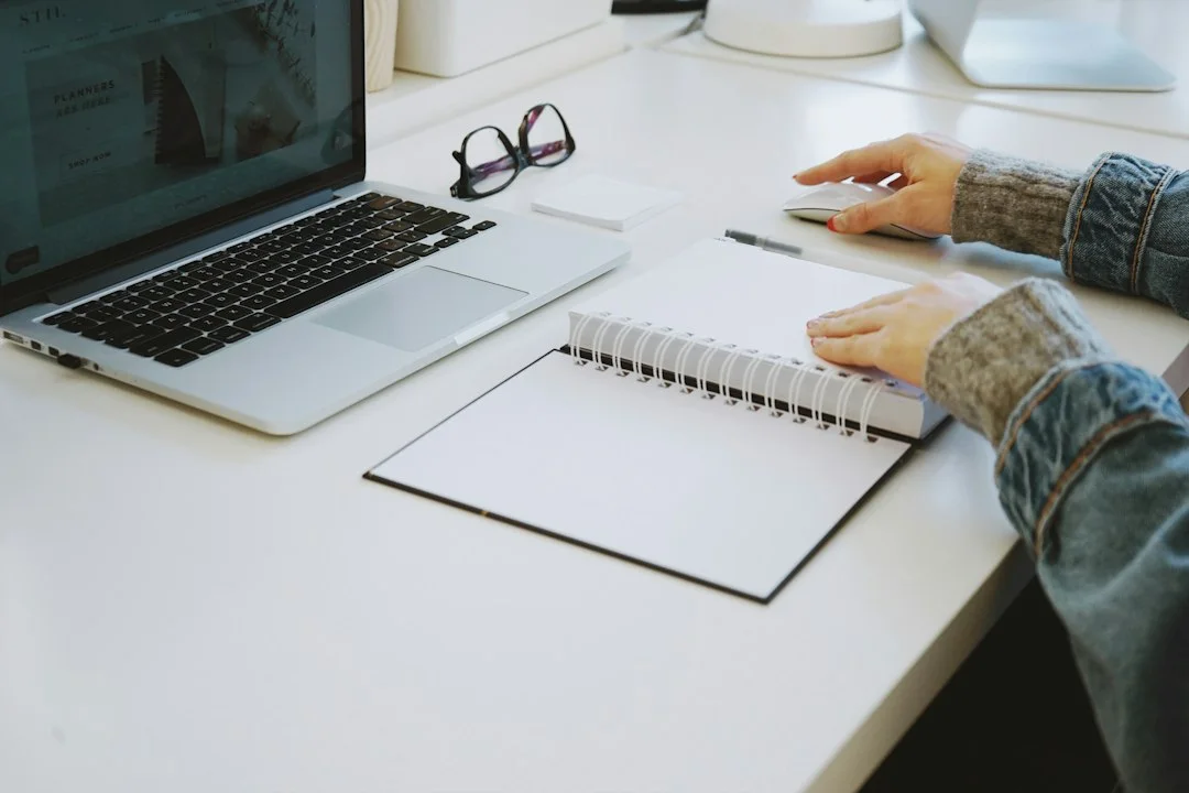 A person reviewing a notebook beside a laptop.