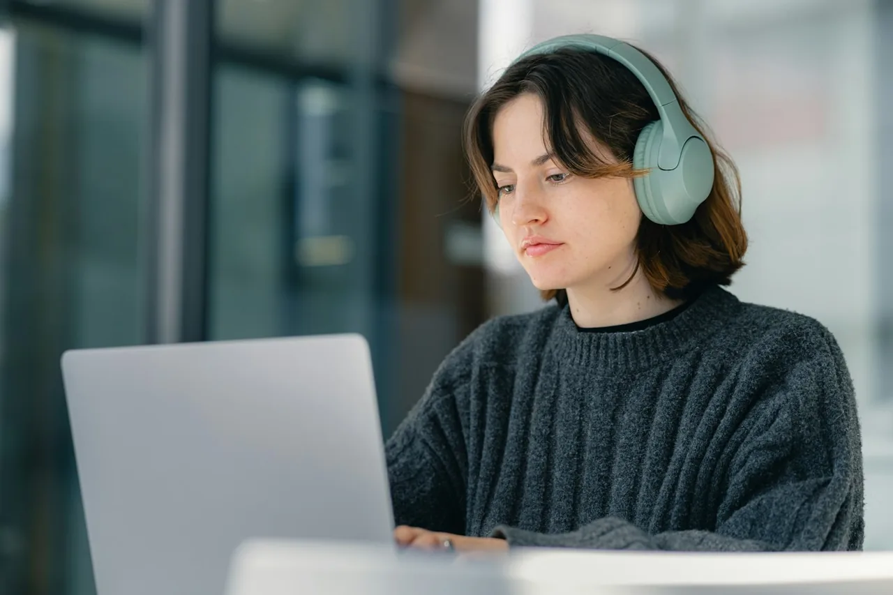 A woman wearing headphones while working at a laptop.