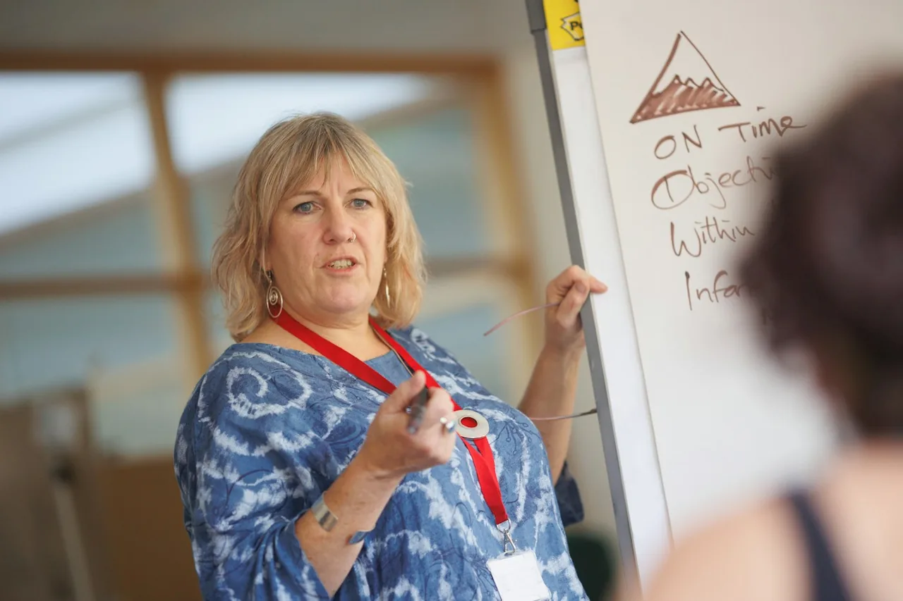 A woman teaching a class with a whiteboard behind her.